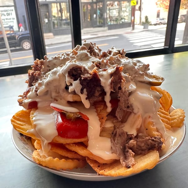 A large bowl of Bar Jawn's waffle fries topped with steak, cheese sauce, and red peppers.