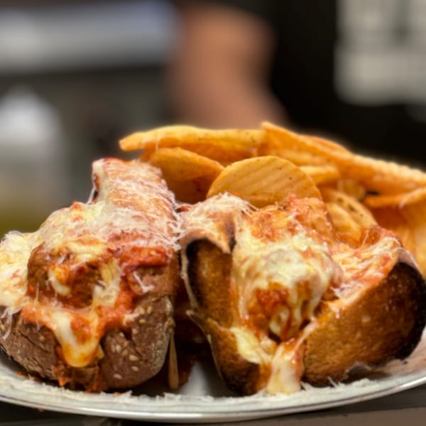 Two meatball subs with melted cheese and marinara sauce, served with crinkle-cut fries.