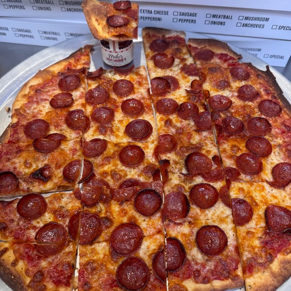 A pepperoni pizza from Bar Jawn, sliced into squares, with a small jar of Mike's Hot Honey.