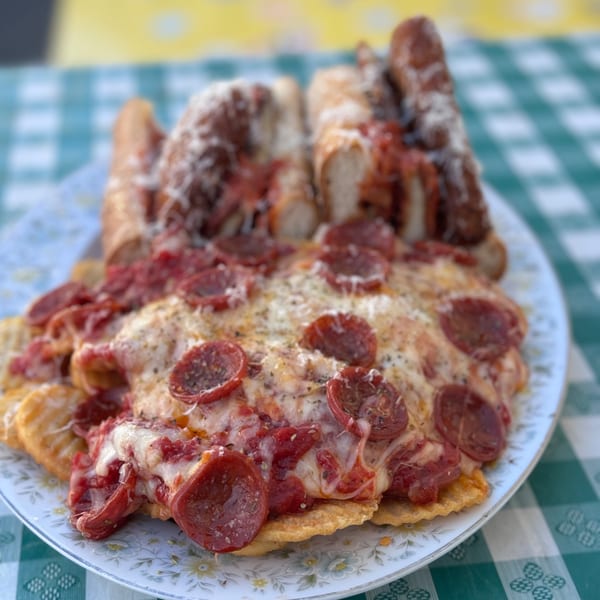 Pepperoni pizza nachos and two meatball subs on a white plate with a green and white checkered tablecloth.