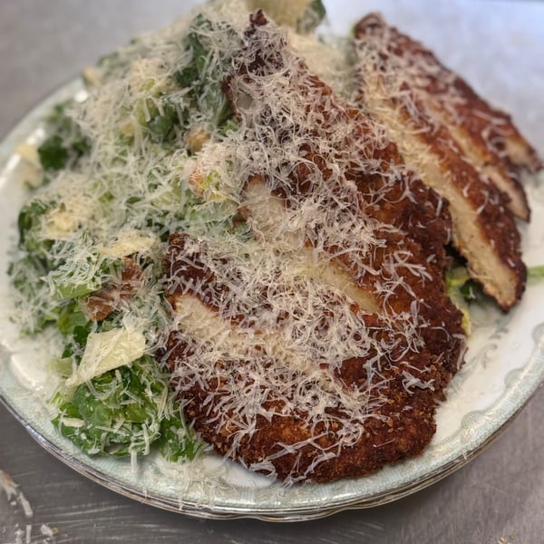 Crispy fried chicken cutlets with Caesar salad, generously topped with shredded Parmesan cheese.