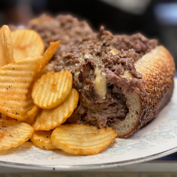 A Bar Jawn cheesesteak sandwich with melted cheese and steak, served with crispy waffle fries.