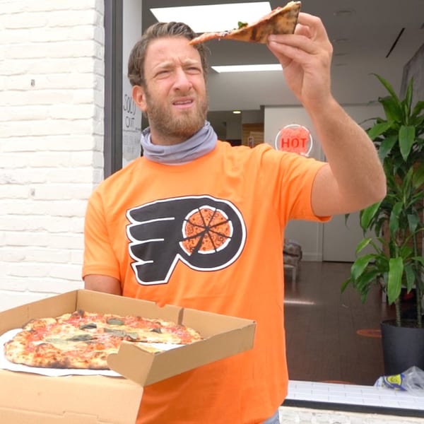Man in orange Bar Jawn shirt holding a pizza box and a slice of pizza.