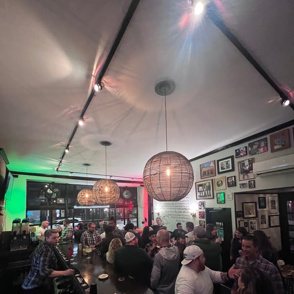 A lively Bar Jawn interior with patrons socializing at the bar under warm, woven pendant lights.