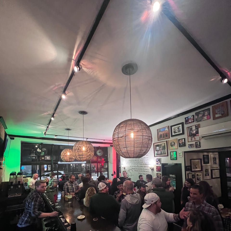 A lively Bar Jawn interior with patrons socializing at the bar under warm, woven pendant lights.