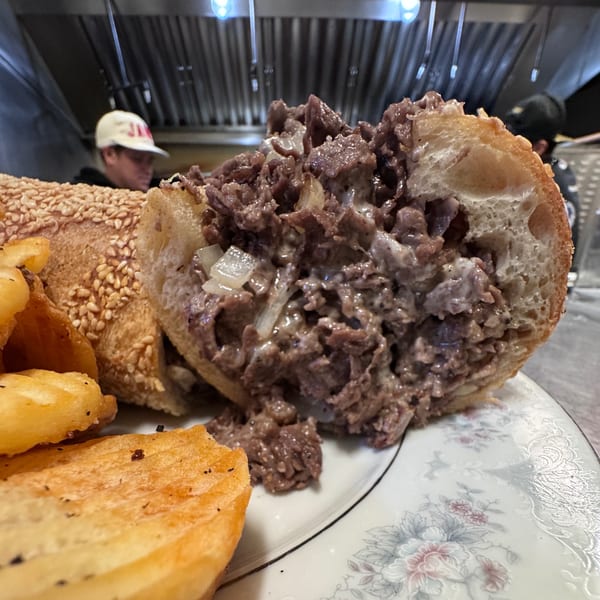 A Bar Jawn cheesesteak with fries on a plate, showing the meaty, cheesy filling and sesame seed bun.
