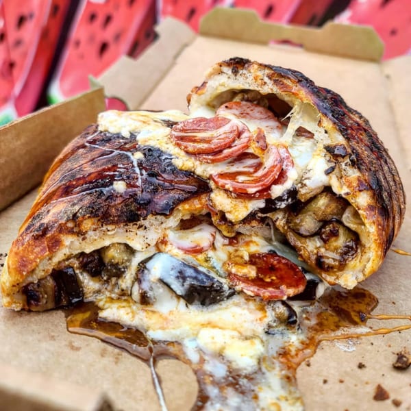 A Bar Jawn calzone, split open, revealing melted cheese, pepperoni, and mushrooms, in a cardboard box.