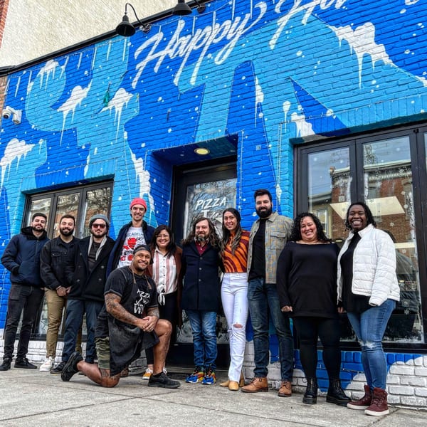 A group of diverse people posing in front of Bar Jawn's vibrant blue and white mural.