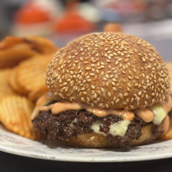 A Bar Jawn burger with melted cheese and sauce, served with crinkle-cut chips.