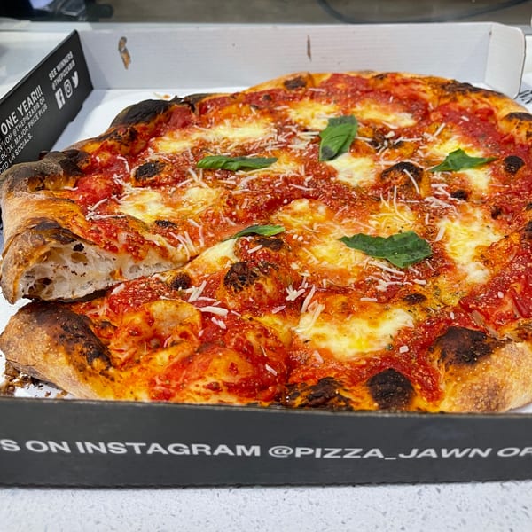 A Bar Jawn pizza with a slice removed, topped with red sauce, cheese, and basil.