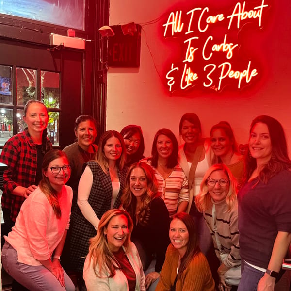 A group of women smiling and posing for a photo under a red neon sign at Bar Jawn.