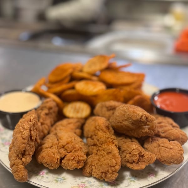 Crispy fried chicken tenders and potato wedges with dipping sauces on a floral plate.