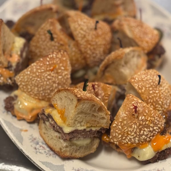 A platter of Bar Jawn's American sliders with sesame seed buns, cheese, and sauce.