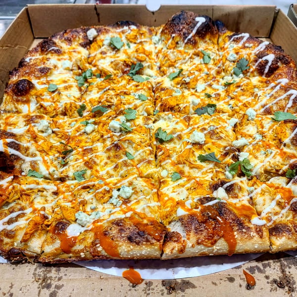 A Bar Jawn buffalo chicken pizza, topped with blue cheese, ranch, and cilantro, in a cardboard box.