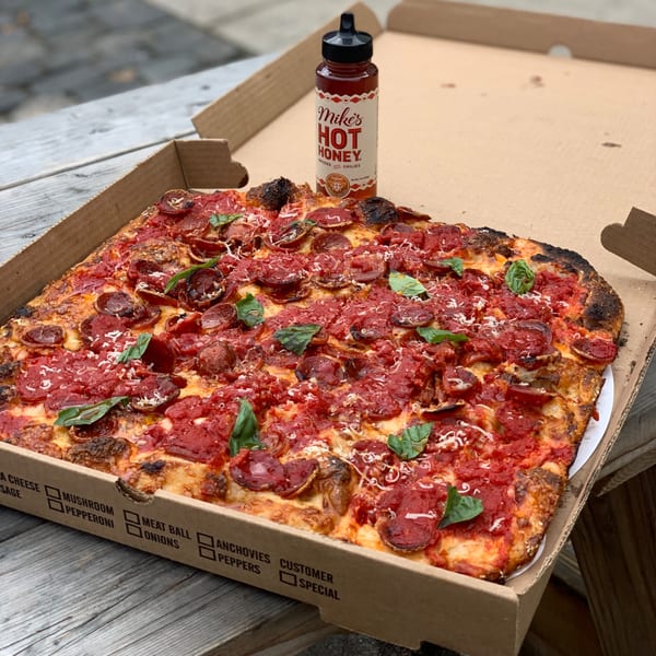 A Bar Jawn pepperoni pizza with basil and Mike's Hot Honey bottle in a cardboard box.